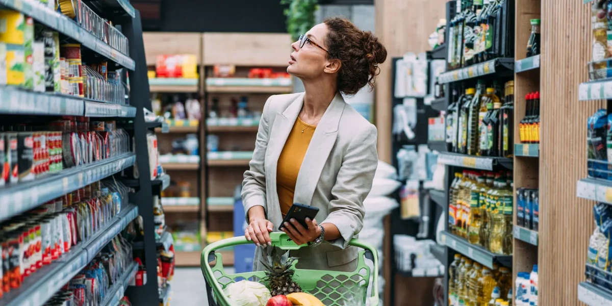 A young woman buying groceries, with her phone in hand