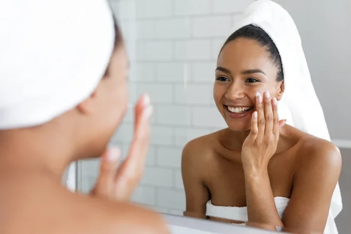 A woman is looking at the mirror and taking care of her skin