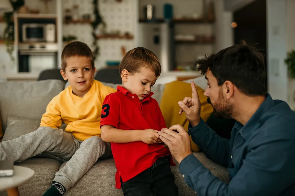 An annoyed man is teaching his son and his brother how to behave while sitting on the sofa at home during the day.