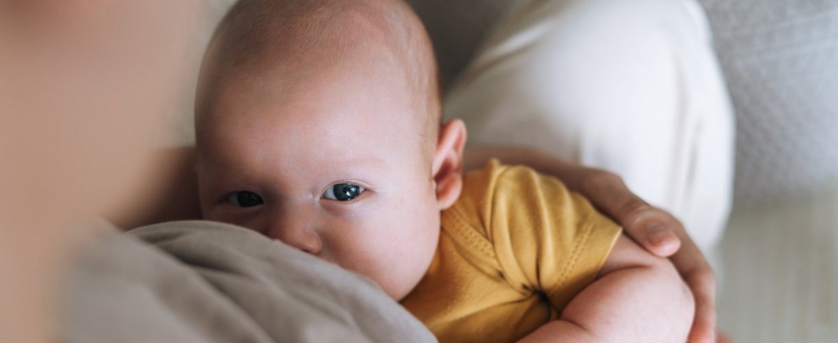 Young mother breastfeeding your 2-3 month baby boy lying on blanket at home