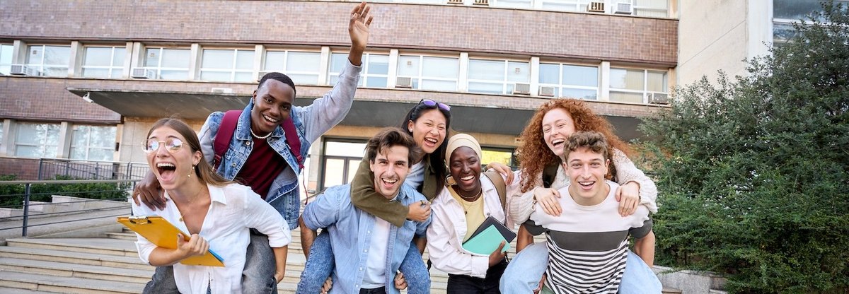 Multiracial group of student friends doing piggyback all together after school, having fun, looking at camera cheerfully.