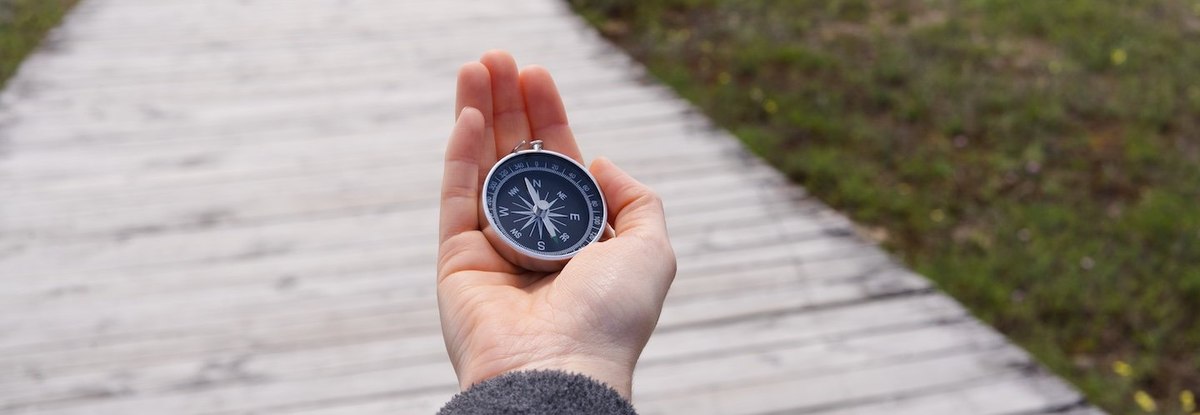 A person holding a compass on a wooden boardwalk.