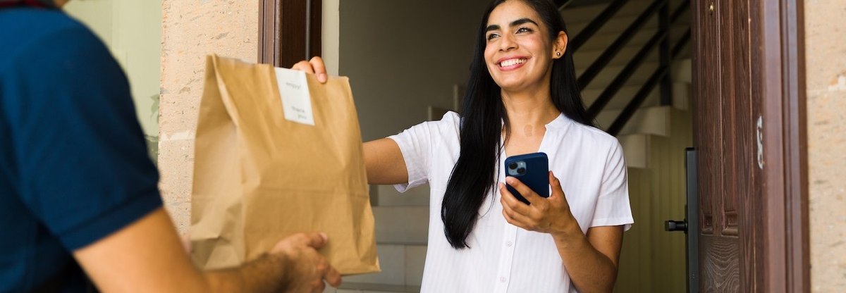 Happy customer receiving a food order at home from a delivery man using a smartphone app