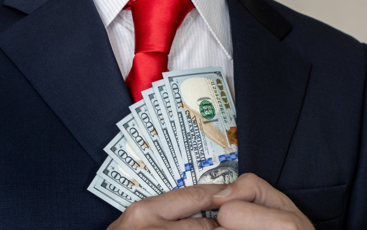 A rich man in a suit and tie counts US dollars in his hand and puts them in his pocket.