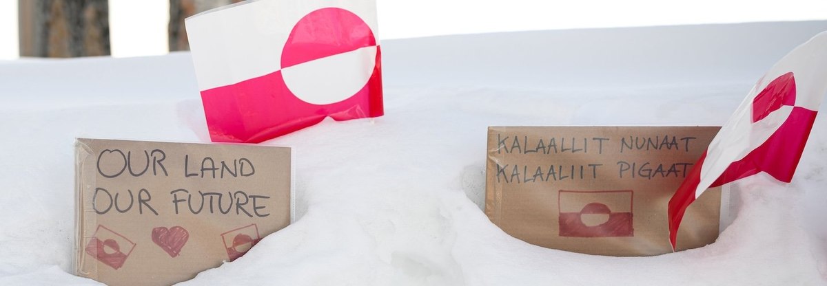 Signs reading "Our Land Our Future" in both English and Greenlandic rest in the snow alongside flags of Greenland, on March 30, 2025 in Nuuk, Greenland.