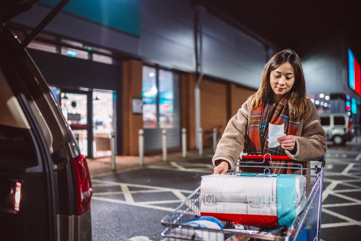 a woman staying close to the car with a shopping cart