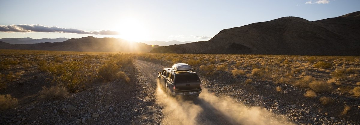 A truck driving down a dusty road towards the sunset in Death Valley.
