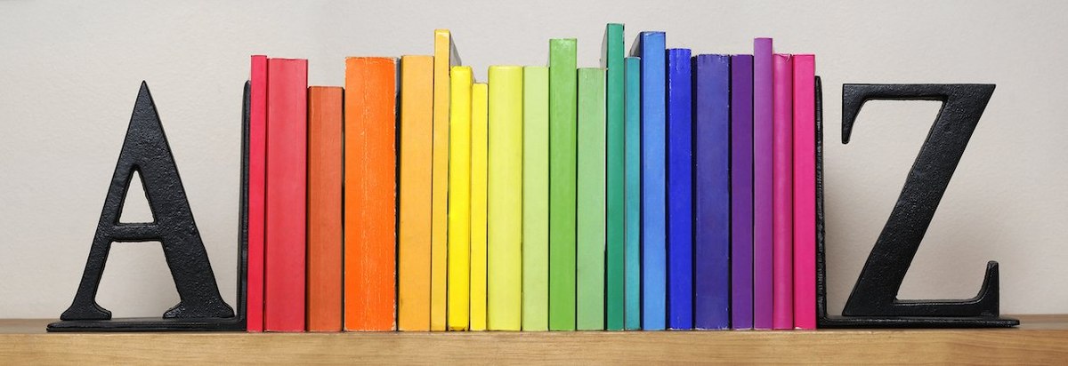 A picture of books on a shelf, arranged by color in a rainbow hue