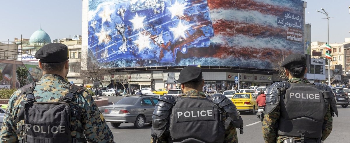 TEHRAN, IRAN - FEBRUARY 21: Anti riot police stand in front of state building that is covered with a giant anti-U.S. billboard depicting the destruction of a US aircraft carrier in downtown Tehran on a main street in Tehran on February 21, 2026 in Tehran, Iran. In recent weeks, the United States has moved vast numbers of military vessels and aircraft to Europe and the Middle East, heightening speculation that it intended to strike Iran. (Photo by Majid Saeedi/Getty Images)