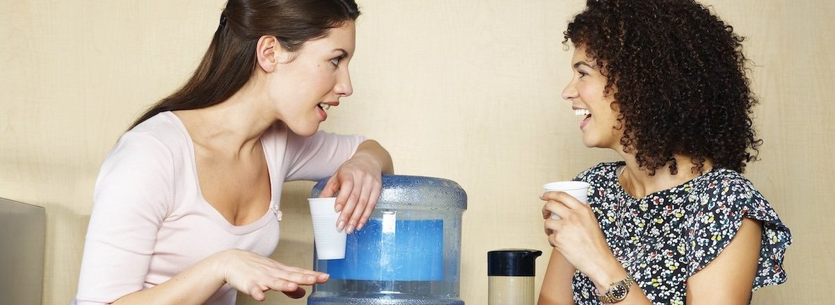 Two women are chatting by water cooler - stock photo Slough, England