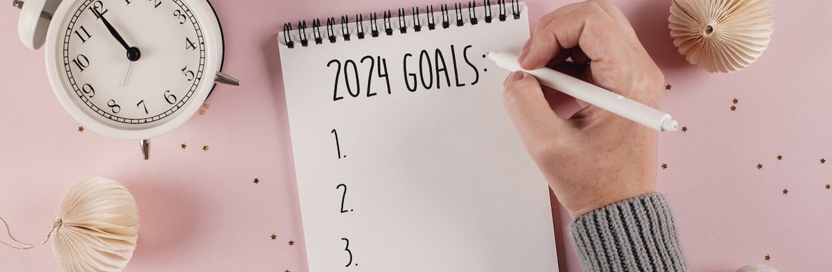 Woman's hand writing goals 2024 for New Year. New Year Routine. Pink background with festive decoration. Flat lay style - stock photo
