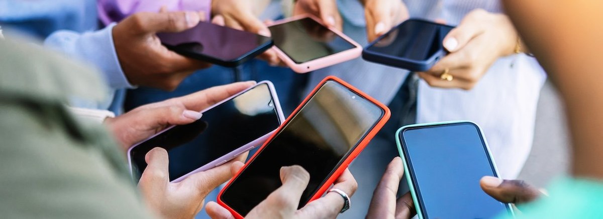 Young group of people standing in circle using mobile phones outside. Unrecognizable teen friends watching social media content on smartphone app. Technology lifestyle concept.